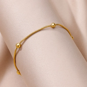 Detail view of gold snake chain anklet with polished beads on silk fabric scroll