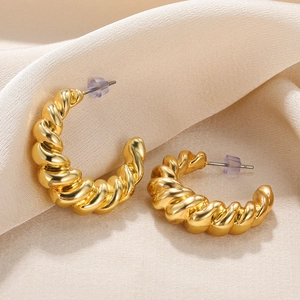 Detailed view of gold-plated croissant earrings with polished texture on silk background