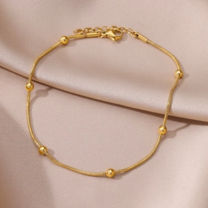 Detail of 18k gold plated snake chain anklet with round beads on champagne silk background