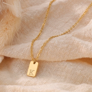 Macro shot of gold square pendant with engraved letter K on stainless steel chain