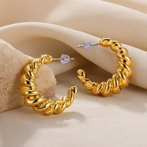 Detailed view of gold twisted croissant earrings on textured stone and beige fabric