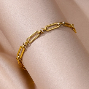 Macro view of gold paperclip link anklet chain on premium champagne satin fabric