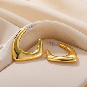 Close-up of gold irregular geometric hoop earrings on soft beige silk fabric