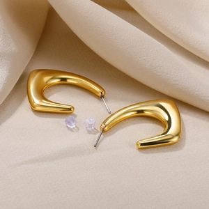 Close-up of golden irregular C-shaped hoop earrings with polished mirror finish on silk