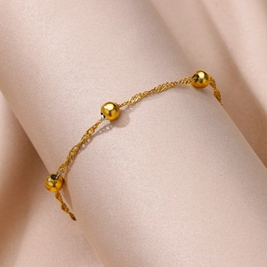 Macro detail of a 18k gold plated stainless steel anklet with beads on champagne velvet