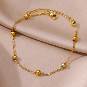 Detail of gold-plated stainless steel anklet with polished beads on satin fabric