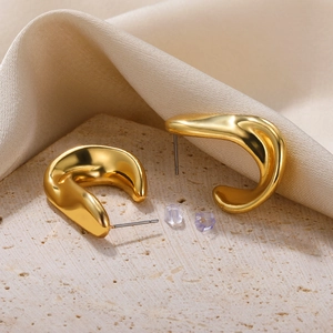 Detailed view of gold C-shaped thick earrings on stone with champagne silk background