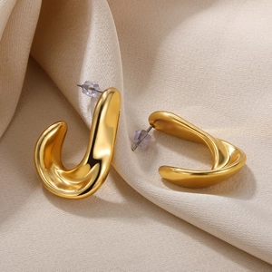 Macro detail of golden twisted C-shaped earrings on elegant beige textured fabric background