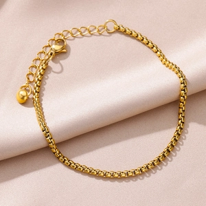 Detail of 18k gold-plated figaro chain anklet with lobster clasp on satin background