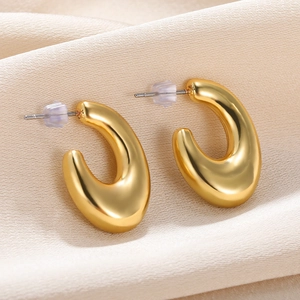 Macro detail of chunky gold drop-shaped C earrings on elegant silk fabric background