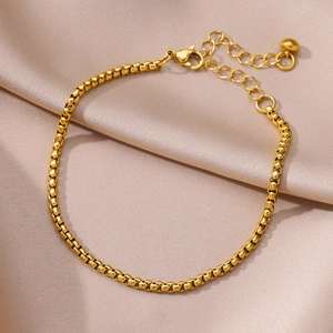 Detailed macro view of a golden box chain anklet on a premium champagne satin background