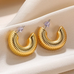 Detailed close-up of golden C-shaped textured earrings on elegant silk background