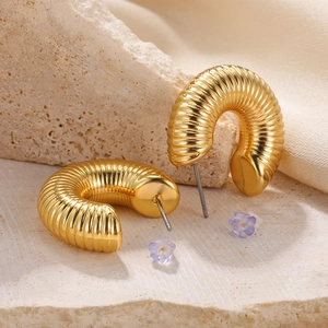 Macro shot of gold textured hoop earrings with silver pins on a beige stone surface