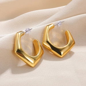 Macro shot of gold geometric C-shaped hoop earrings with polished finish on beige fabric