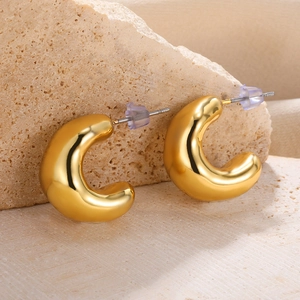 Close-up of golden chunky C-shaped hoop earrings resting on natural stone with metal pins