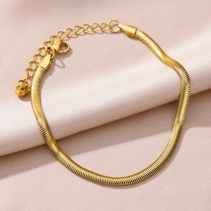 Macro detail of gold-plated snake chain anklet with lobster clasp on pink silk fabric