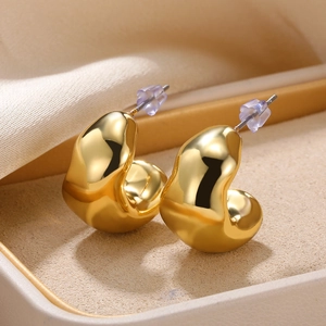 Macro shot of polished gold C-shape stud earrings on cream velvet with silicone backings