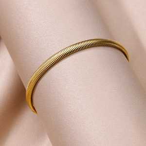 Macro shot of gold-plated snake chain anklet on a premium champagne silk background