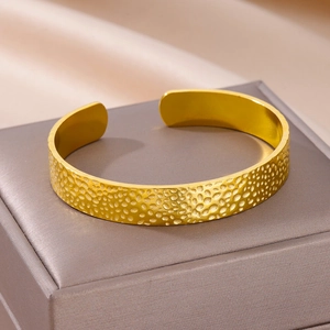 Close-up van een gouden open armband met gehamerde textuur op een luxe sieradendoos