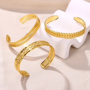Detailed view of three gold-plated open bangles with geometric hollow patterns on white props
