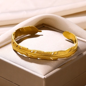 Detailed close-up of golden feather texture on an adjustable stainless steel cuff bracelet