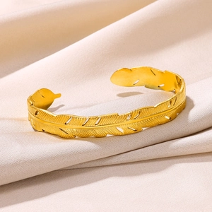 Macro shot of gold feather-shaped open bangle with intricate brushed texture details