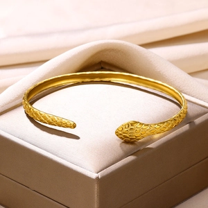 Detailed view of gold snake-shaped open bangle with intricate scale texture on a jewelry box