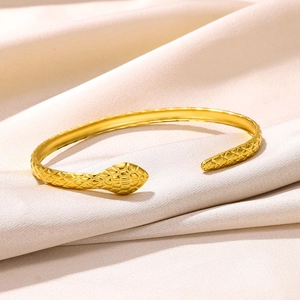 Detailed view of golden snake-shaped bangle with scale textures on champagne satin fabric