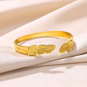 Close-up of golden feather open cuff bracelet with detailed texture on silk background
