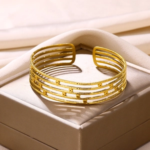Detail of multi-layer gold plated open cuff bracelet with small circular beads on a silk box