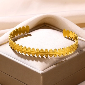 Detail of golden stainless steel cuff bracelet with leaf-like textures on satin fabric