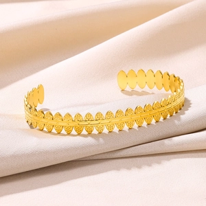 Detail of gold-plated stainless steel leaf pattern cuff bracelet on beige satin
