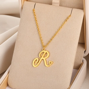 Détail d'un collier doré avec pendentif lettre R et cœur évidé dans son écrin