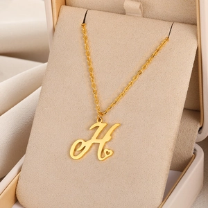 Vue détaillée du pendentif lettre H doré avec motif cœur dans un coffret à bijoux beige