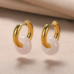Detailed shot of golden hoop earrings with translucent natural stone charms on beige fabric