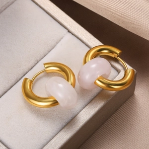 Detail of elegant gold hoop earrings with light pink natural stone on gray velvet padding