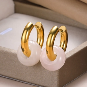 Macro shot of gold hoop earrings with white gemstone donut pendants on beige jewelry box