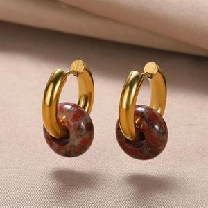 Detail view of gold hoop earrings with reddish-brown marble stone beads on fabric