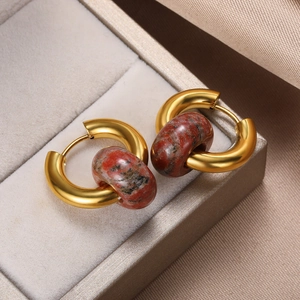 Macro shot of gold-plated hoop earrings with red marble stone charms on neutral fabric