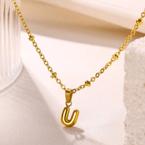 Detailed close-up of 18K gold plated bubble letter U pendant on a fine beaded cross chain