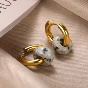 Close-up of gold donut hoop earrings with natural spotted stone on beige silk fabric