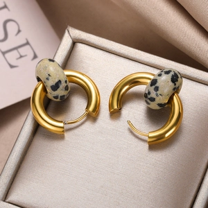 Detailed close-up of golden donut hoop earrings with spotted natural stone texture