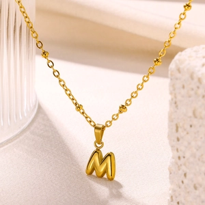 Detailed macro of 18K gold bubble letter M pendant with satellite bead chain necklace