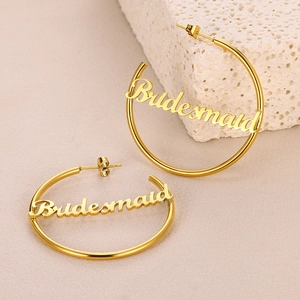 Detailaufnahme goldener Creolen mit Bridesmaid Schriftzug auf einem eleganten Steindekor
