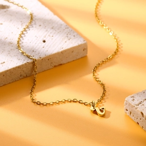 Dettaglio di una collana dorata con pendente lettera U e piccolo cuore su base in pietra