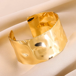 Detailed macro view of wide gold titanium steel cuff with hammered texture on white fabric