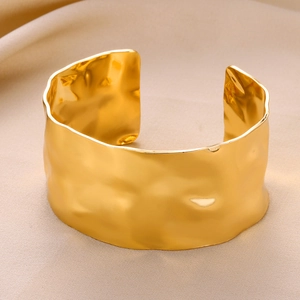 Detail shot of golden wide cuff bracelet with irregular hammered texture and wavy edges