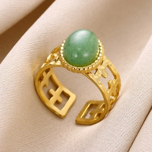 Detailed close-up of 18K gold open ring with green stone on champagne silk background