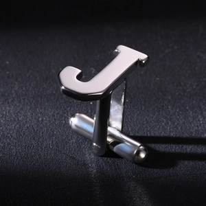Polished silver stainless steel letter J cufflink on textured black surface background