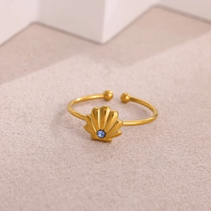 Dettaglio di un anello a conchiglia dorato con una piccola gemma blu centrale
